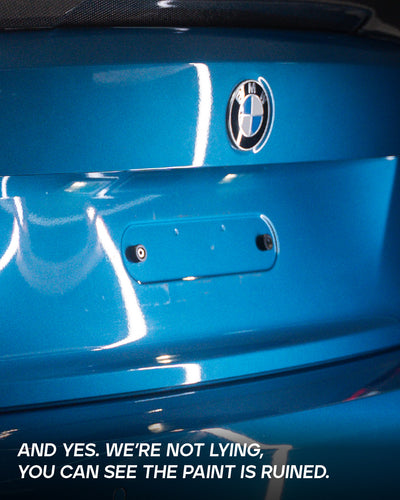 Paint scratches and discoloration on blue BMW rear bumper from a traditional screw-mounted license plate holder